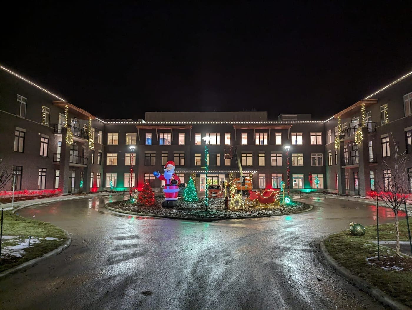 Apartment complex courtyard with a large inflatable Santa and lit Christmas trees framed by warm-white roofline lights