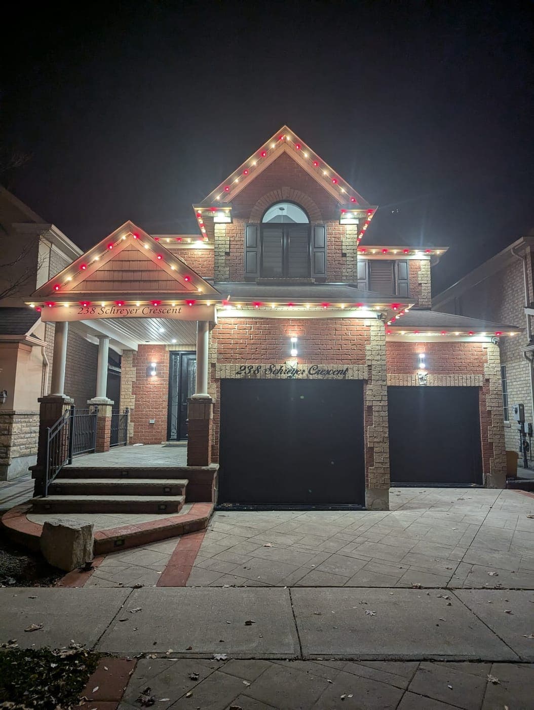Front view of a brick house outlined in warm-white and red C9 roofline Christmas lights at night