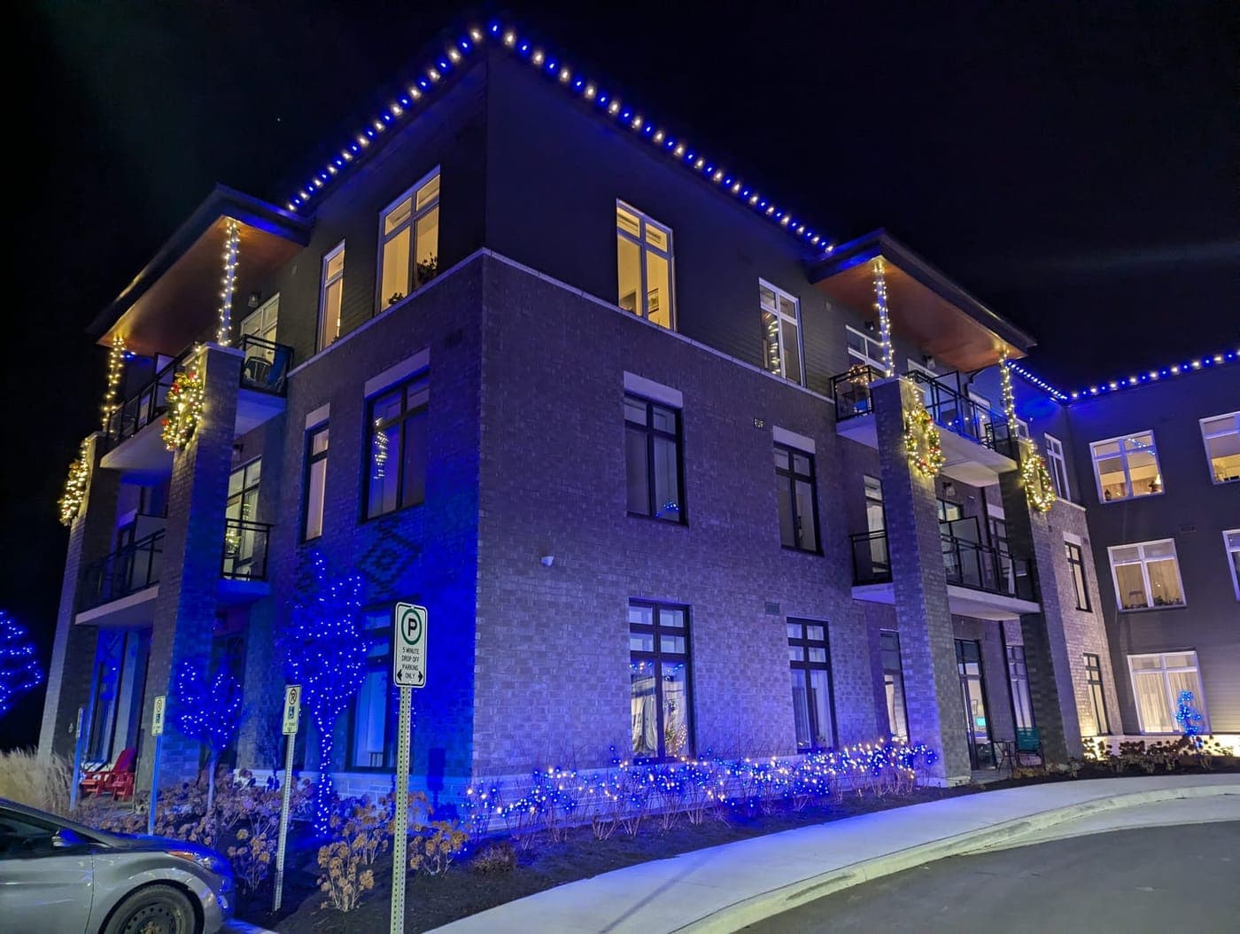 Corner of a commercial building lit with blue roofline lights and warm-white column garland at night
