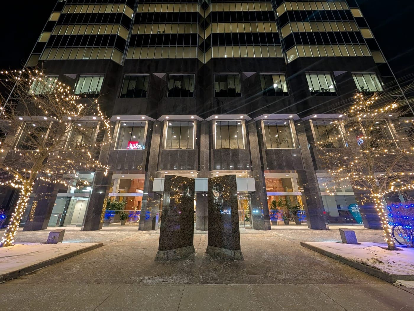 Production Sets: Commercial office building facade with entrance trees wrapped in warm-white lights and blue accent uplighting.