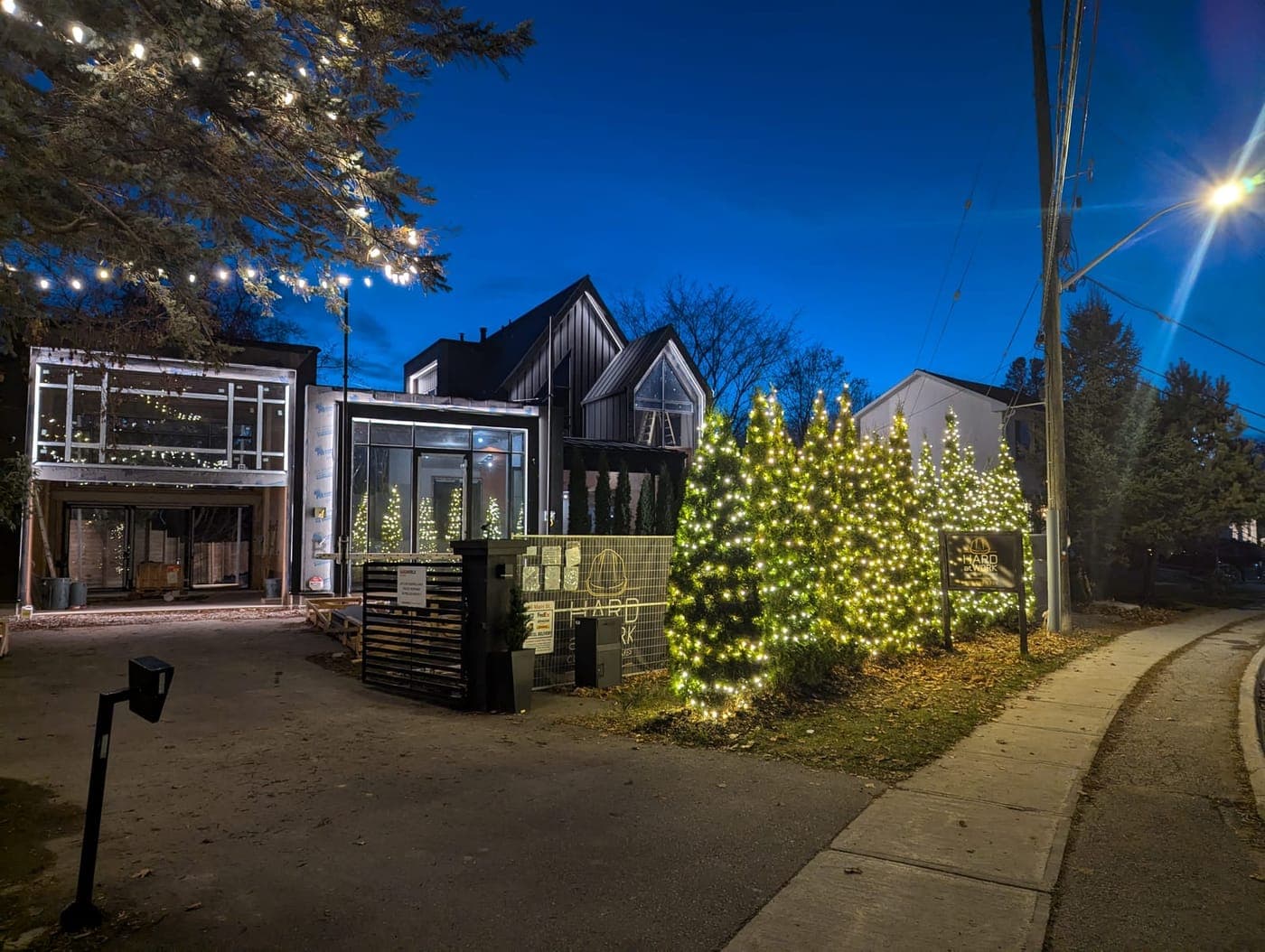 Modern commercial building with patio bistro string lights beside lit cone trees and a tall evergreen
