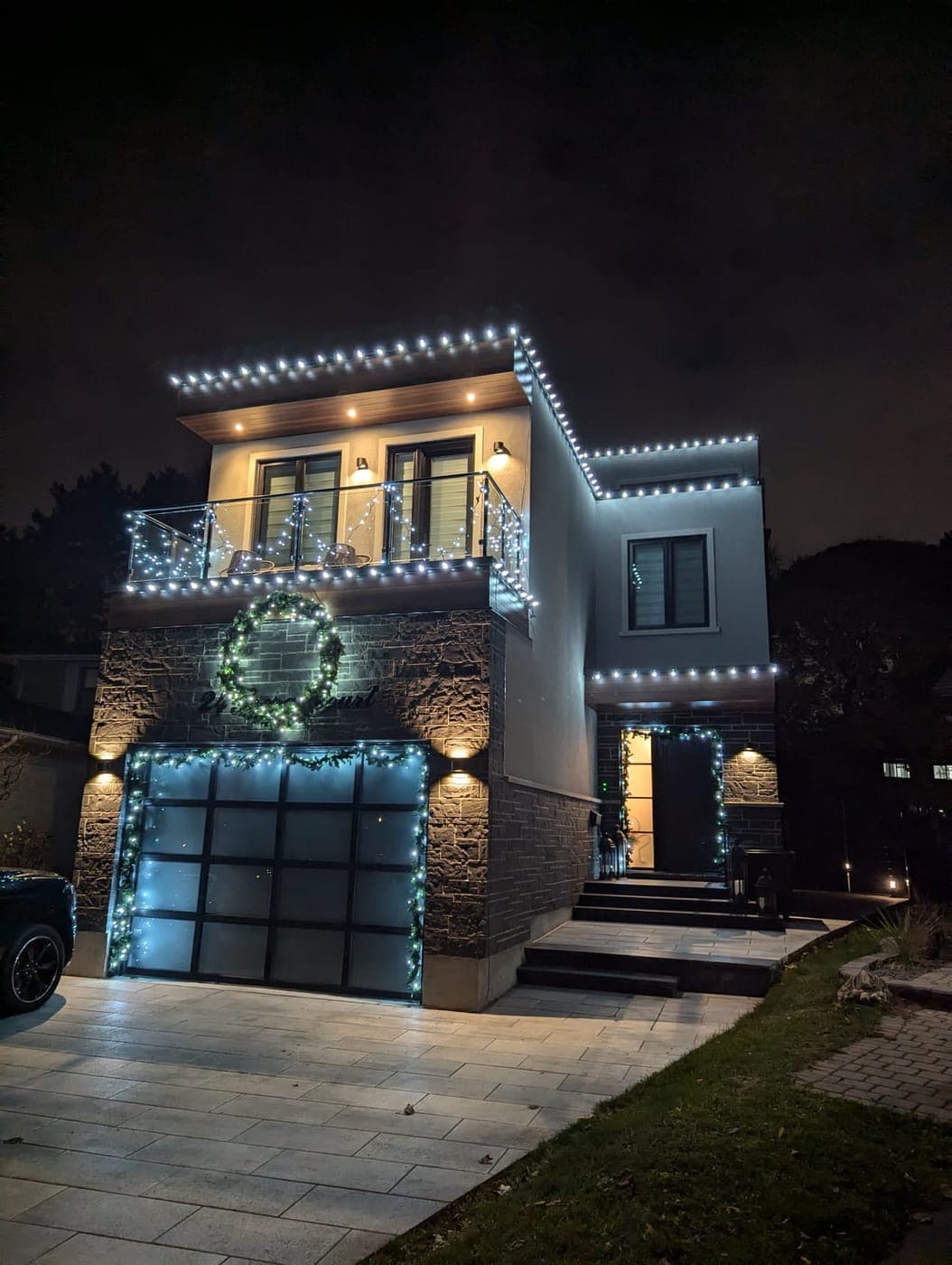 Contemporary home lit with white LED Christmas lights, a glowing wreath and garage garland
