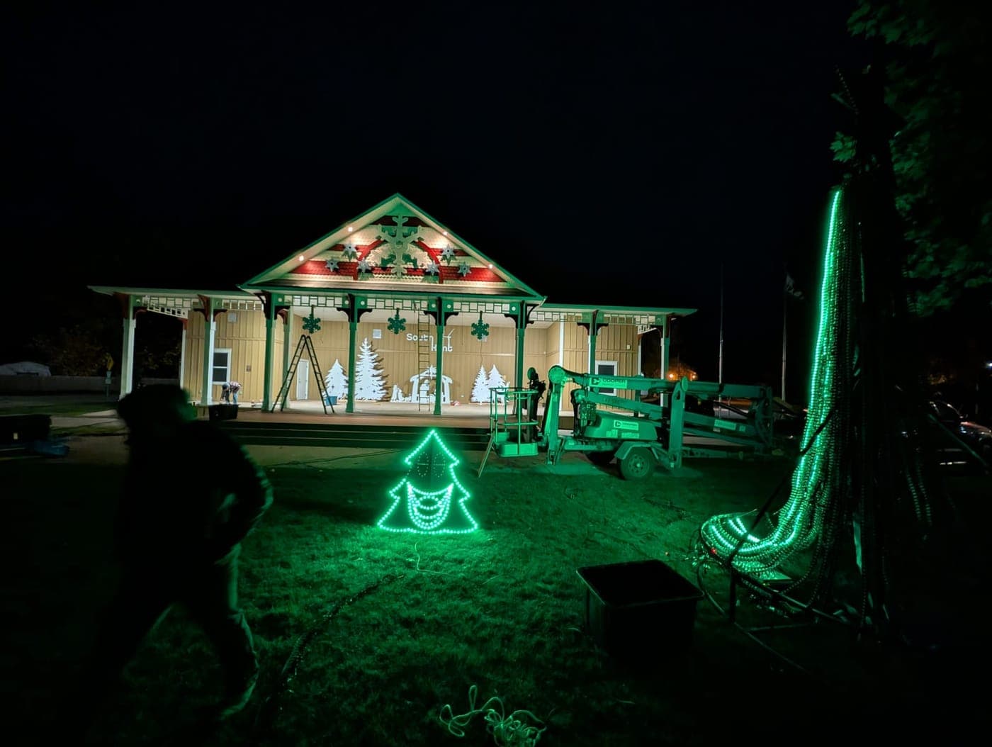 Crew installing Christmas lights and LED displays at a park pavilion at night.