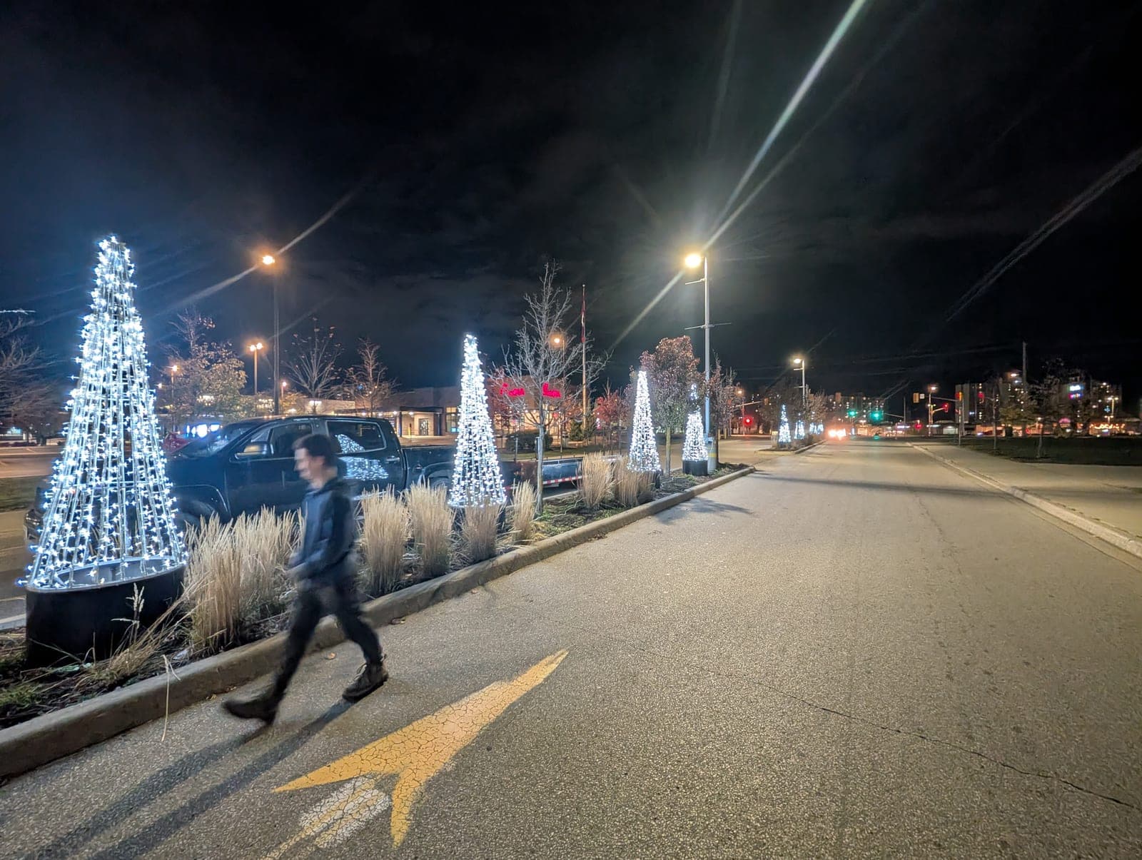 Illuminated cone-shaped Christmas trees lining a commercial boulevard median at night.