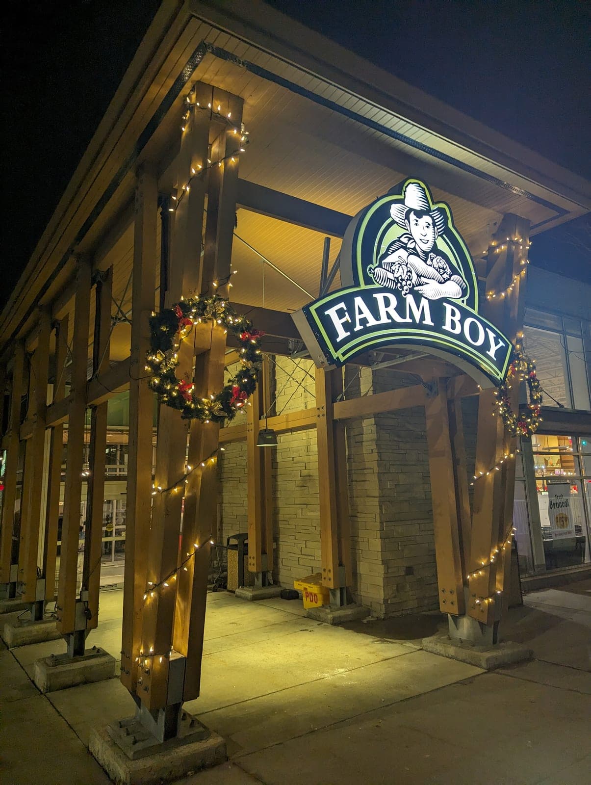 Commercial storefront entrance wrapped in warm-white Christmas lights with an illuminated wreath at night