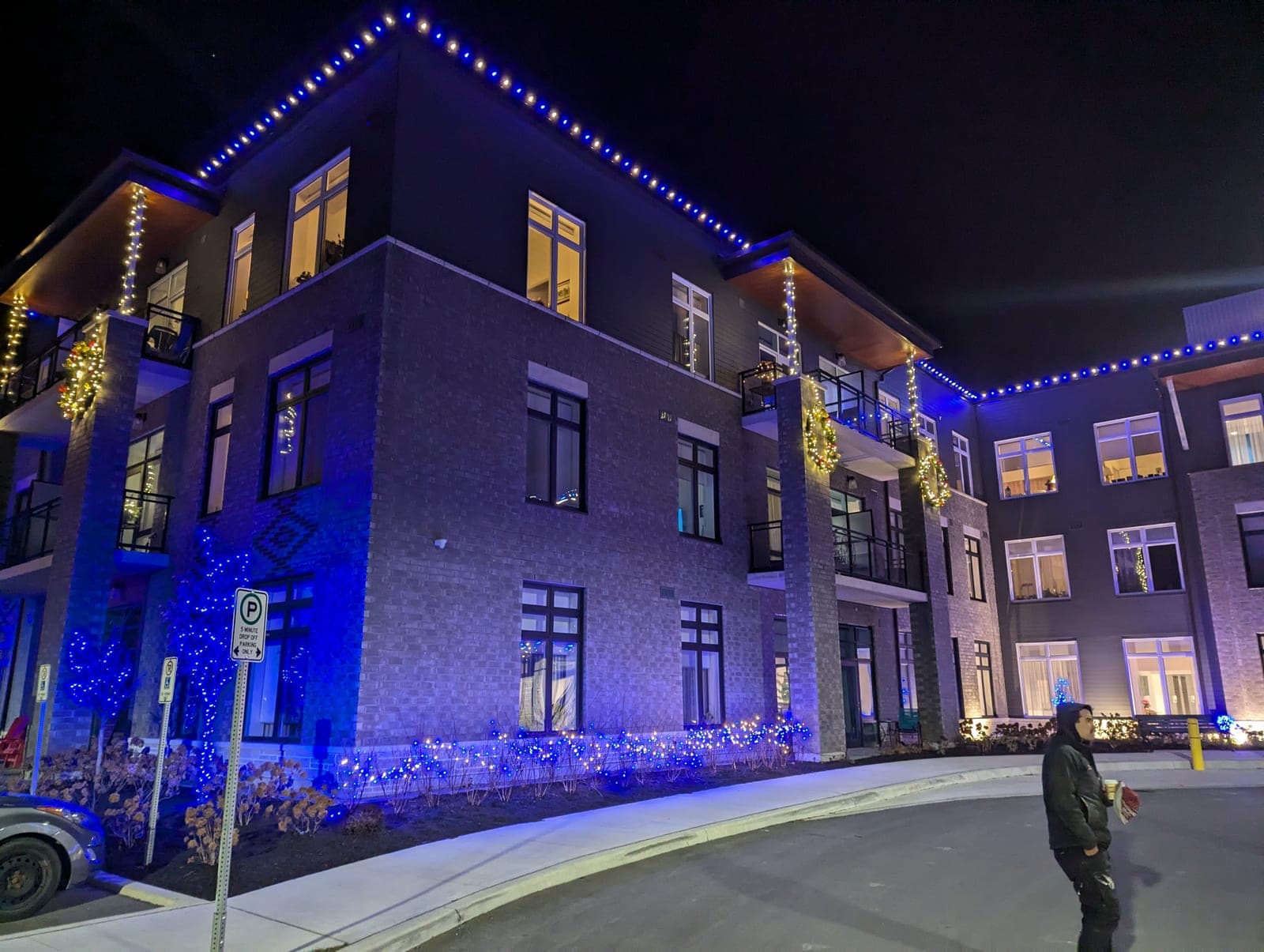 Multi-storey condo building outlined in blue and warm white Christmas lights at night.