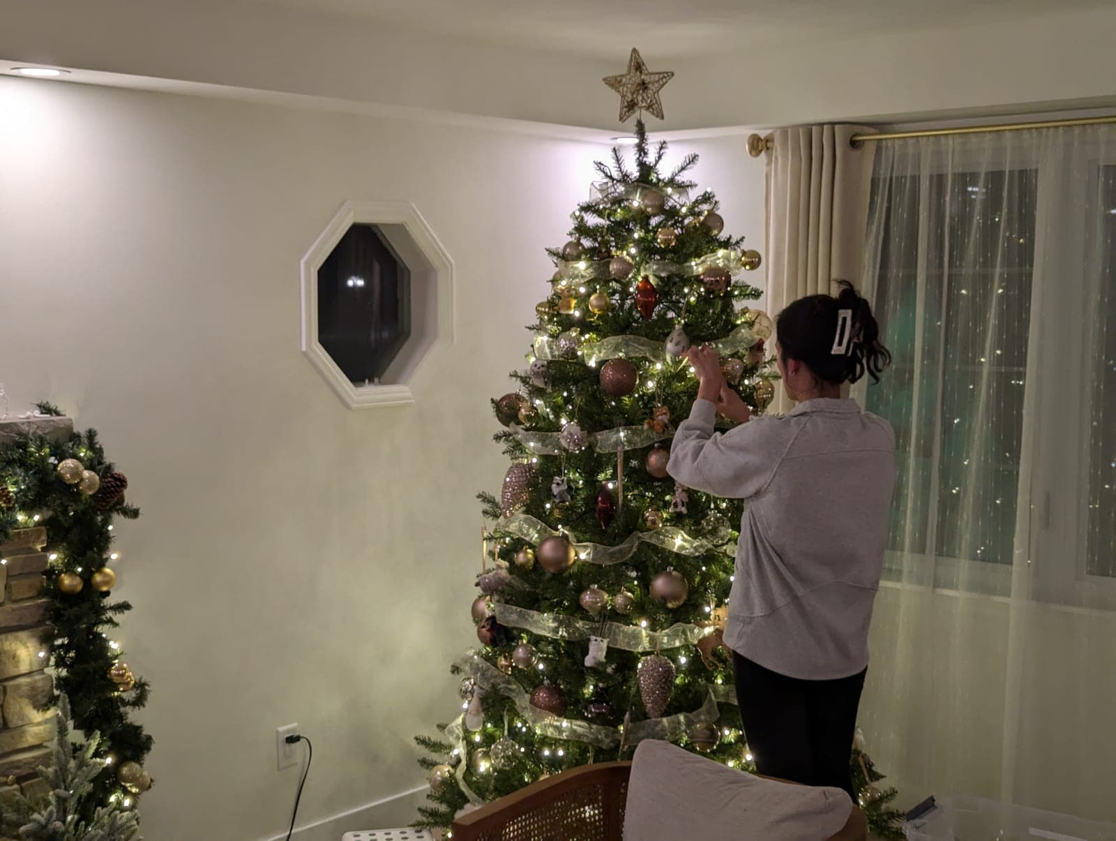 Person decorating an indoor Christmas tree with ribbon and warm white lights.