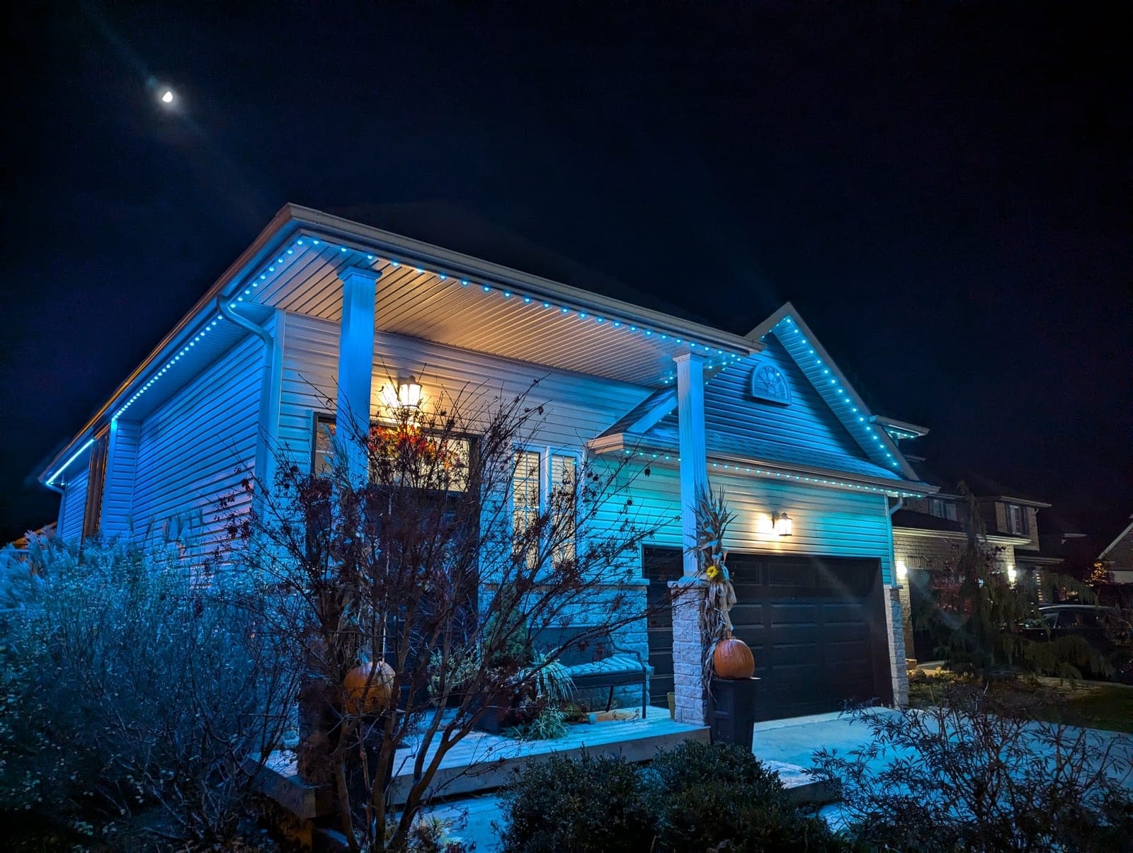 Home outlined in blue permanent LED roofline lights under a moonlit sky