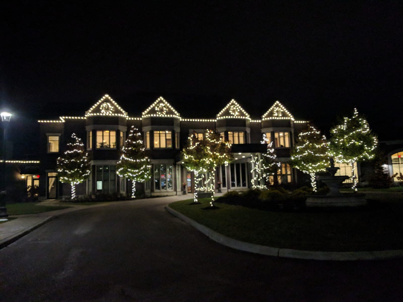 Estate venue at night with warm-white roofline lights and softly lit landscape trees.