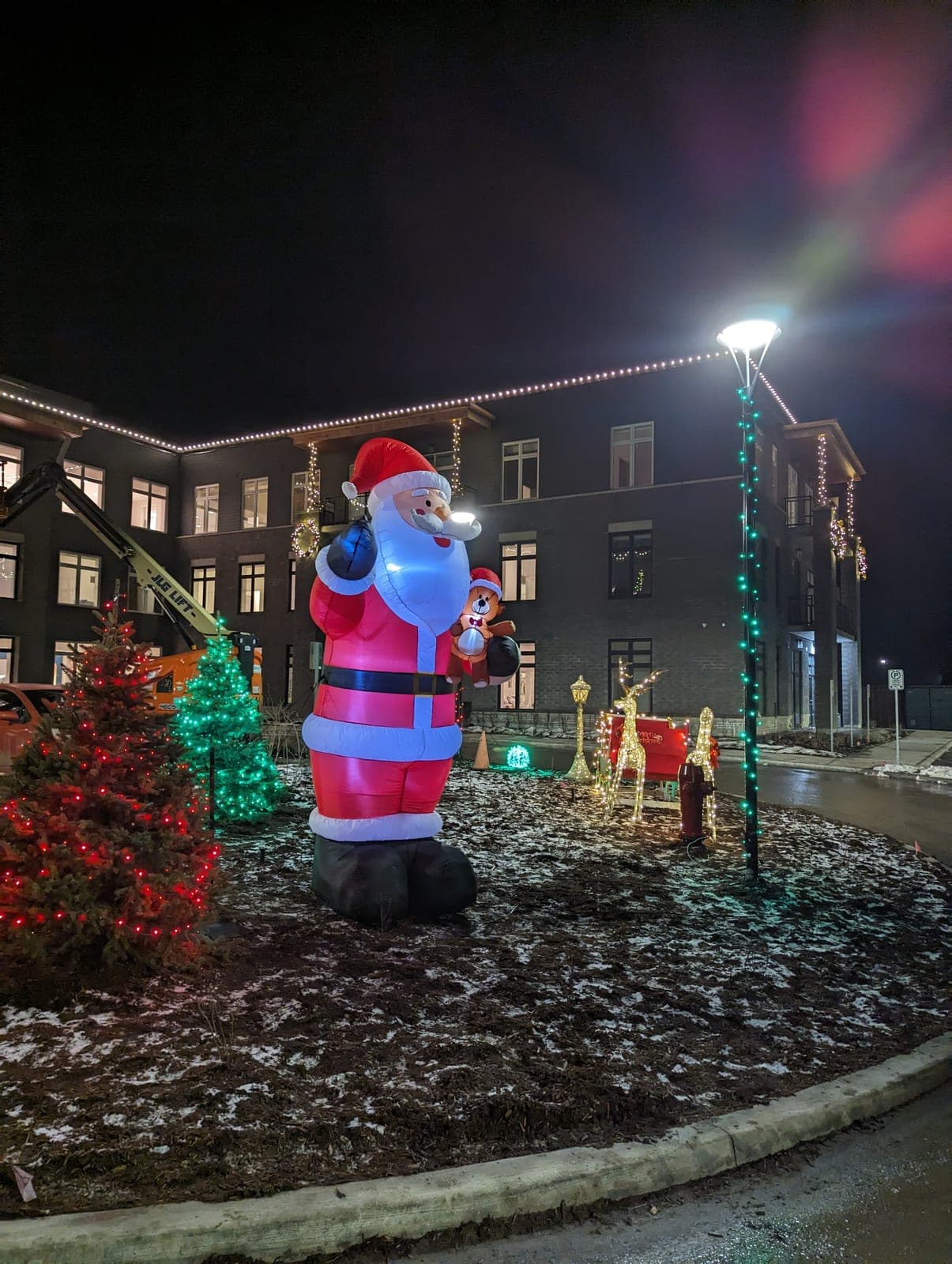 Illuminated giant inflatable Santa and lit trees in front of a commercial building with warm-white roofline Christmas lights