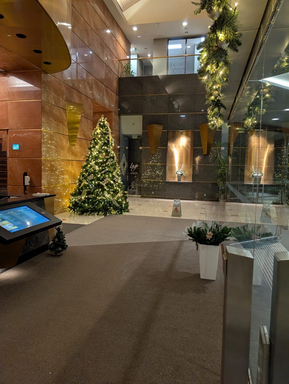 Warm-white lit Christmas tree and matching wall garland in a modern corporate office lobby.