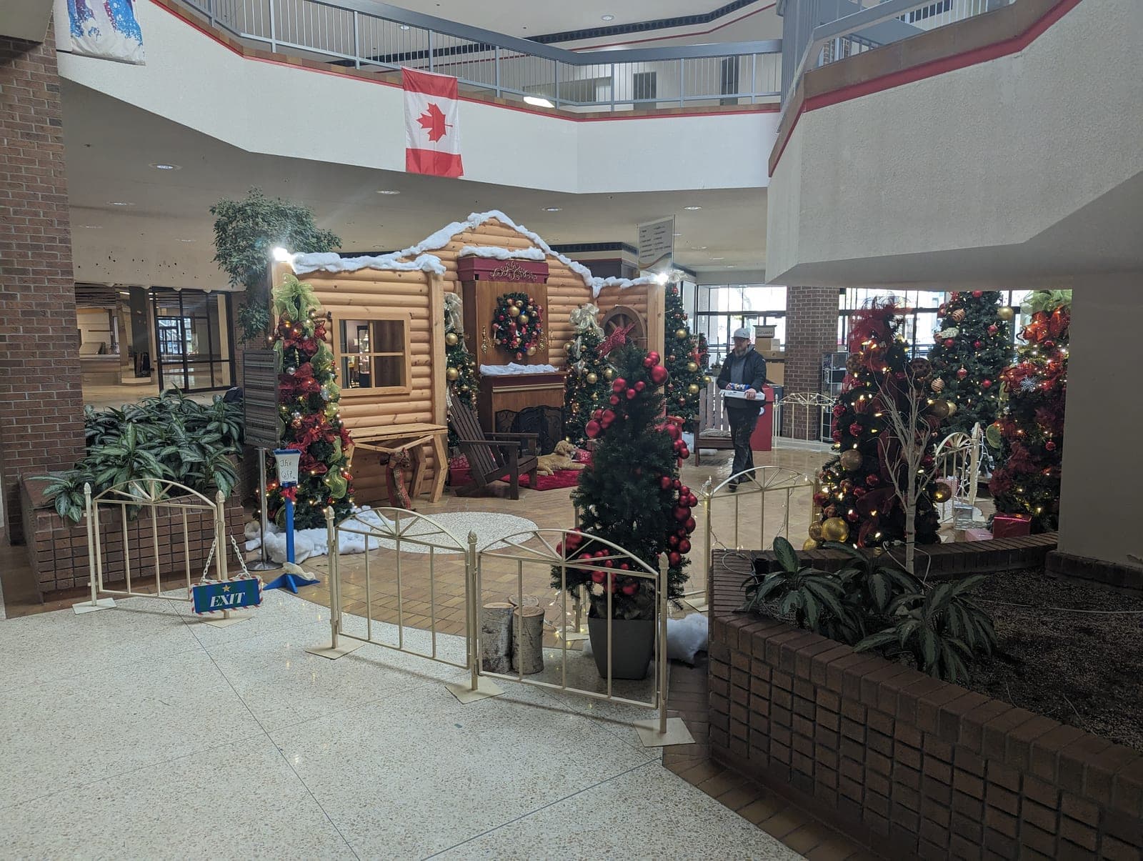 Decorated Christmas village display with lit trees and garland in a shopping mall atrium.