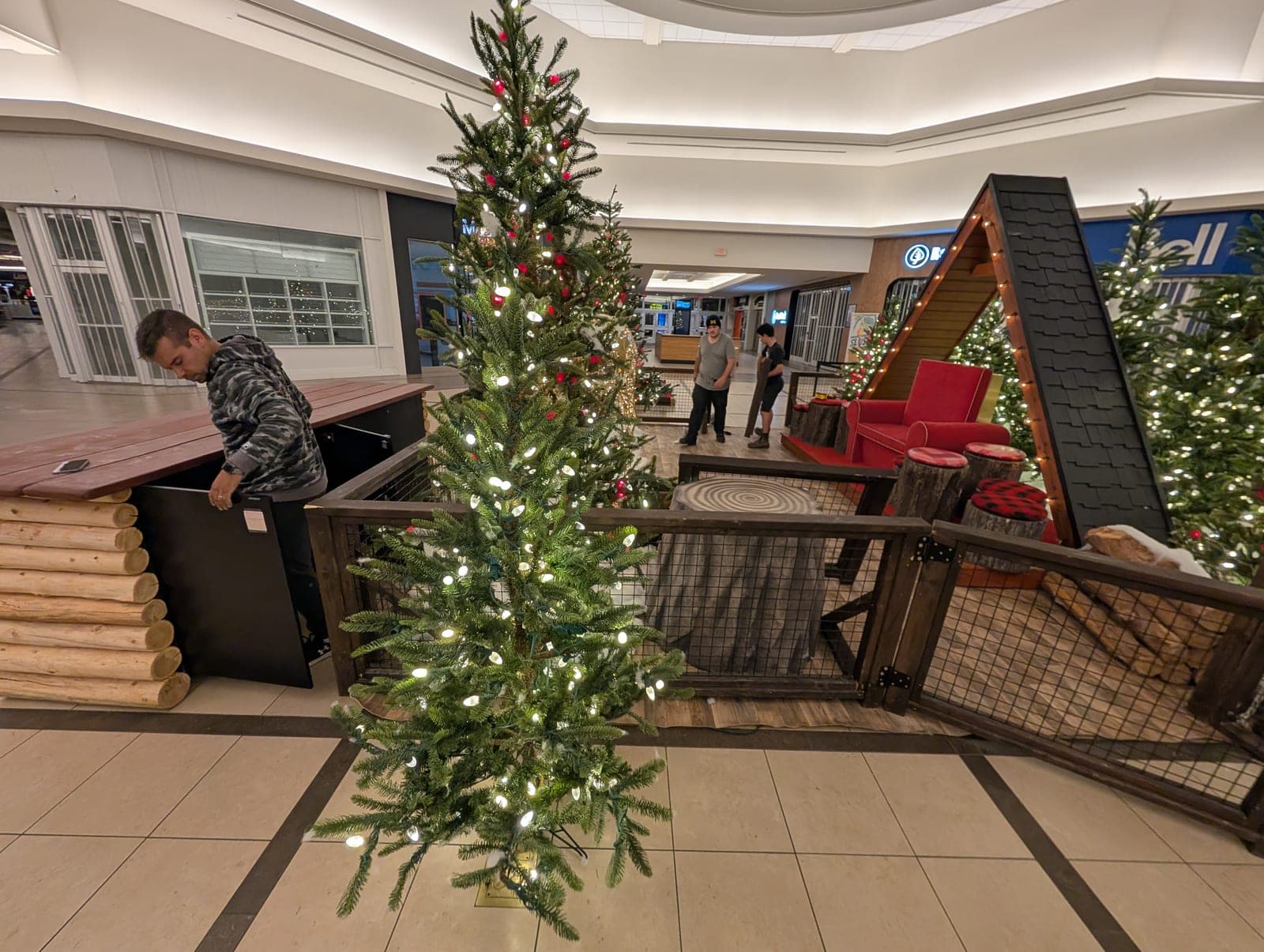 Installation crew setting up a lit Christmas tree display in a shopping mall.