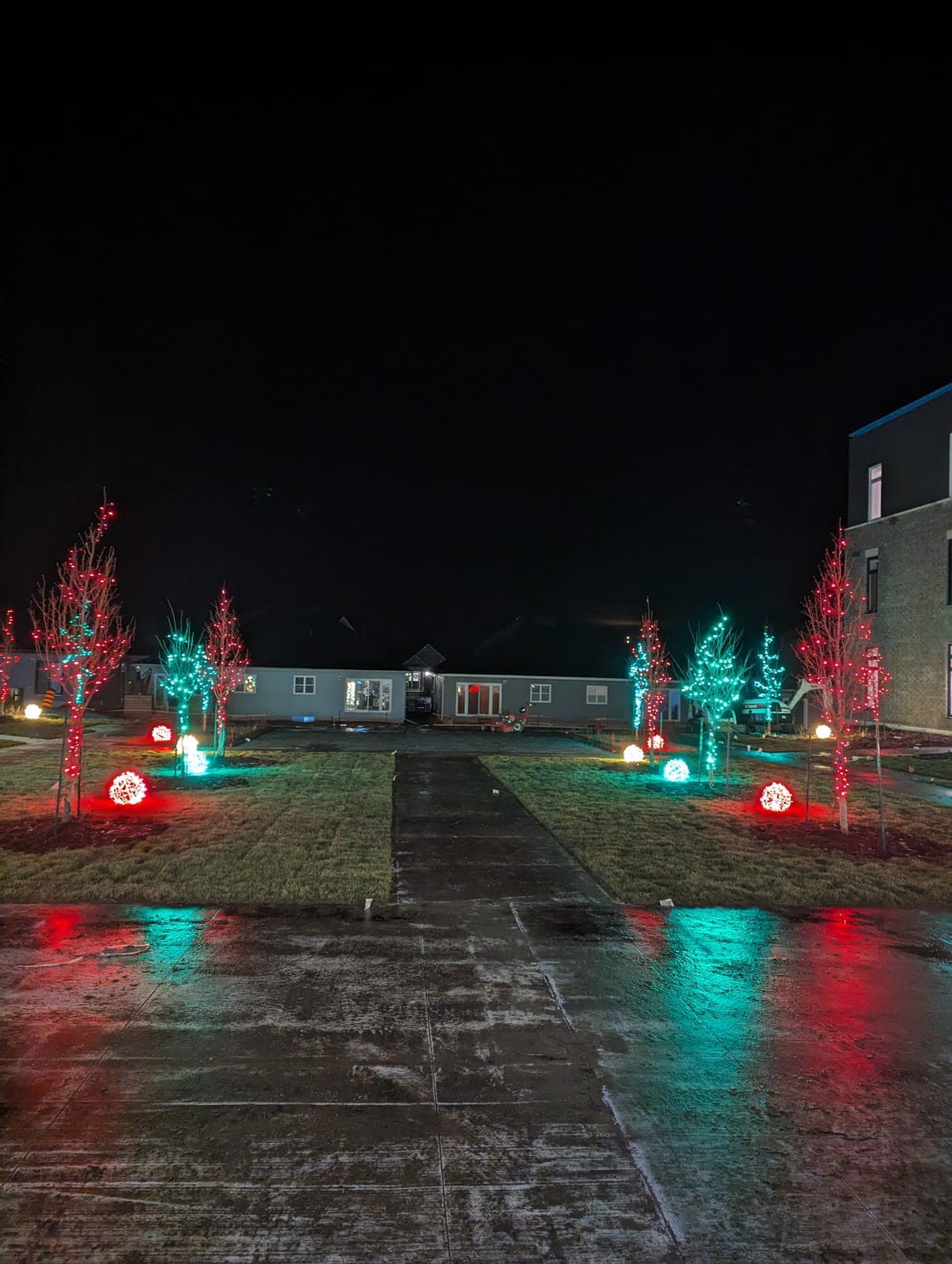 Red and green lit Christmas trees and glowing light spheres lining a commercial courtyard walkway